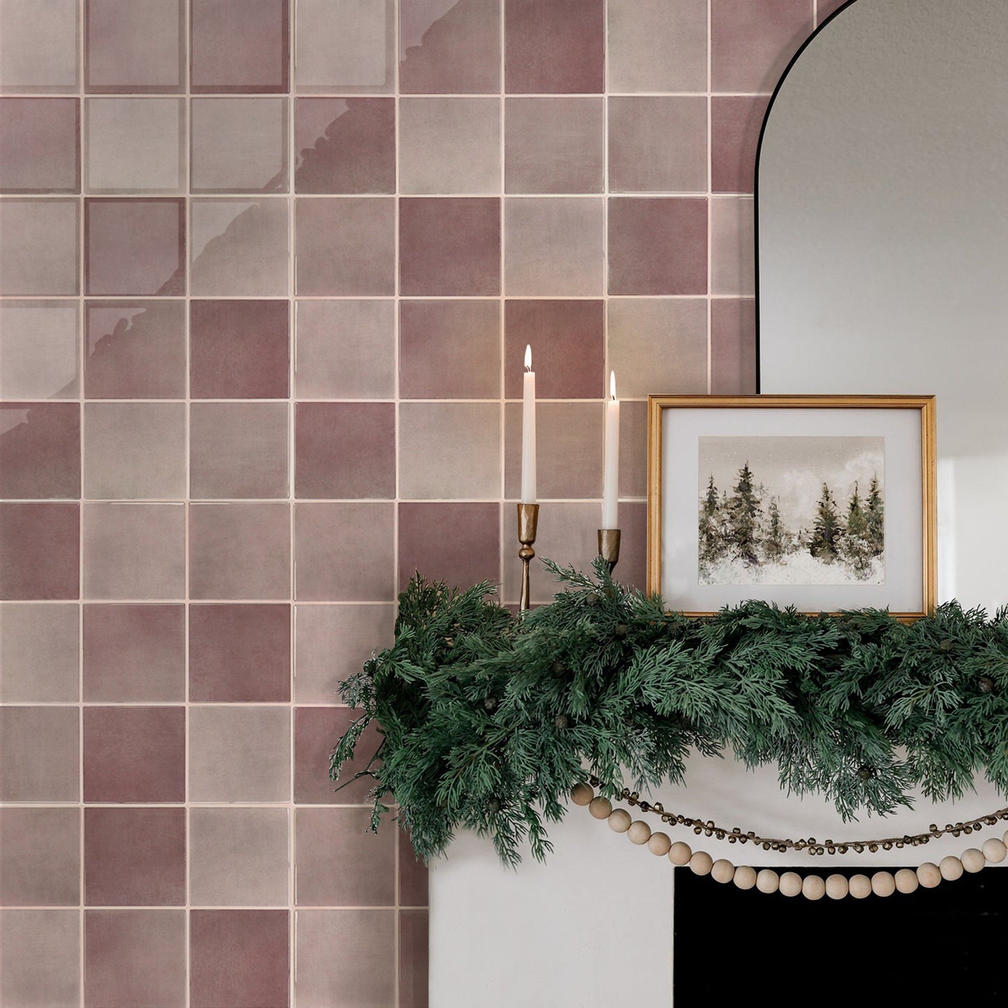Decorative fireplace with greenery, candles, and a framed picture against a tiled wall.