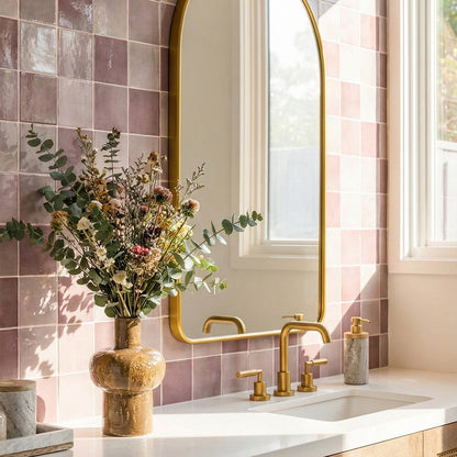 Bathroom with pink tiled walls, gold fixtures, and a vase of flowers.