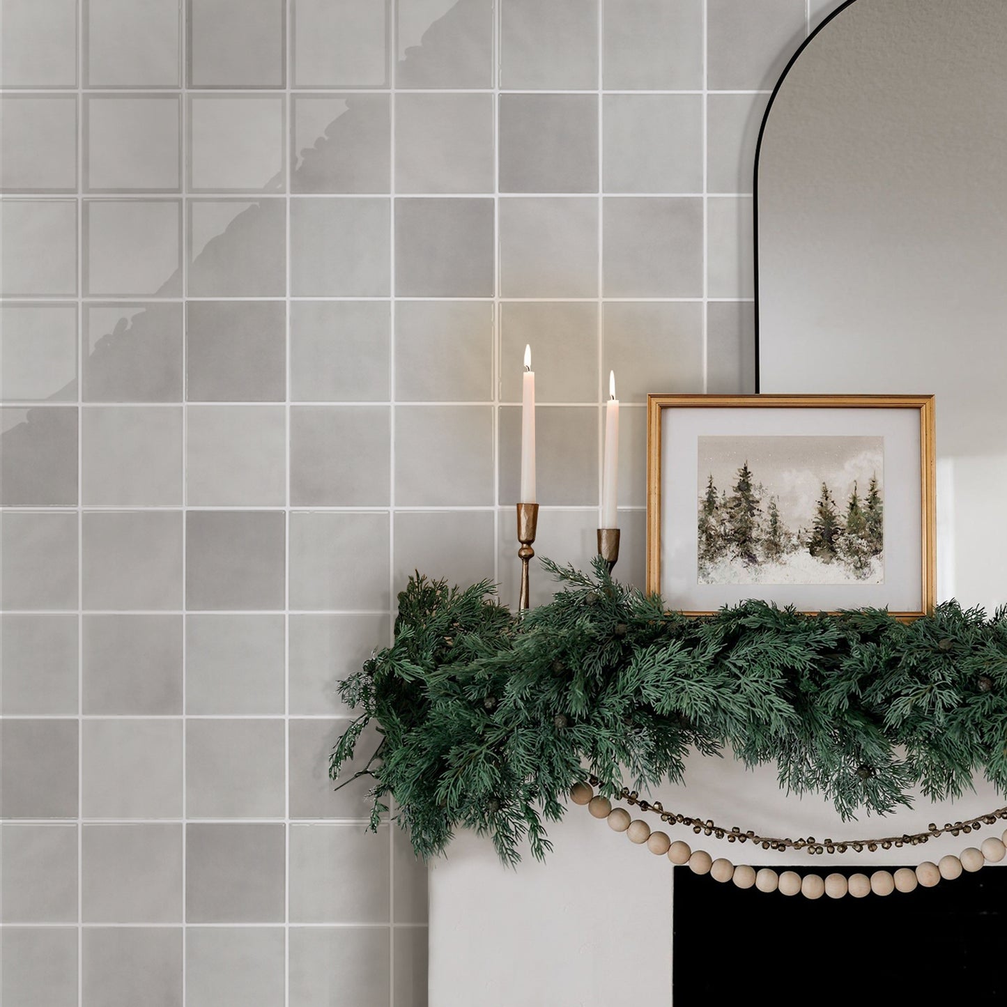 Decorative mantel with greenery, candles, and a framed picture against a tiled wall.