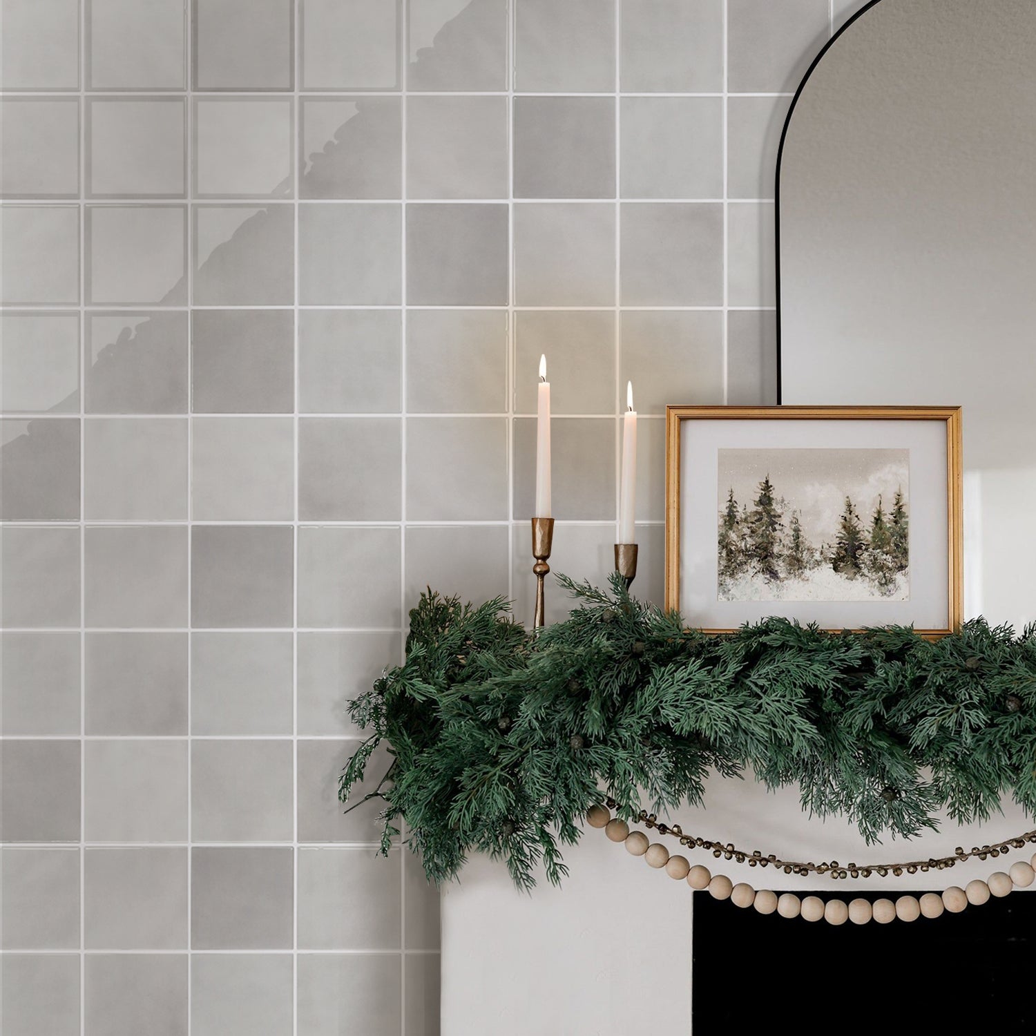 Decorative mantel with greenery, candles, and a framed picture against a tiled wall.